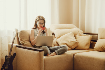 Young woman drinking coffee while using laptop at home.