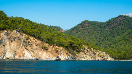 Beautiful deep sea with small waves and steep cliffs on the shores of the Mediterranean Sea with trees and caves.