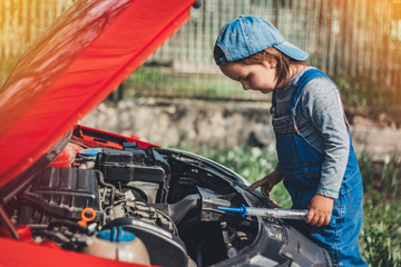 Fototapeta na wymiar Little child trying to fix broken real car. Dreaming to be auto technician