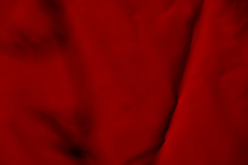 The texture of the synthetic red fabric with pleats. Background of red synthetic shiny fabric