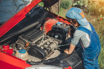 Little child trying to fix broken real car. Dreaming to be auto technician