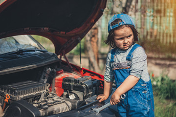 Little child trying to fix broken real car. Dreaming to be auto technician