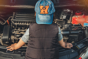 Little child trying to fix broken real car. Dreaming to be auto technician. View from the back