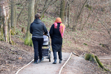 Couple with a baby stroller walking in spring park. Quarantine in a city during covid-19 coronavirus pandemic, concept of motherhood, parents with pram