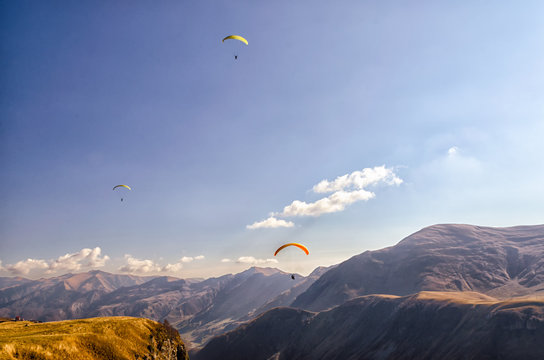 three paragliders in sky against the background of Caucasus mountains