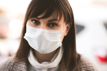 Young sick asian girl 24-26 year old wearing medical mask outdoors posing in city street. Looking at camera. Coronavirus. Social distancing. Quarantine epidemic time. Stay home. Healthcare.