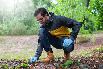 A young bearded man with brown hair and prescription glasses looks through the wilderness for specimens to collect for a study