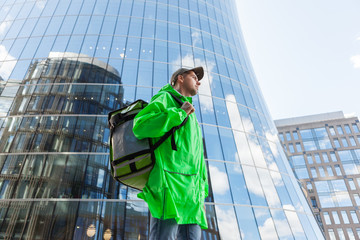 Side view three quarter length shot of male food courier in green uniform walking down city street...