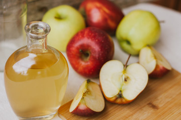 Apple organic vinegar in glass pitcher with ripe fresh red and yellow apples on wooden background. Healthy organic food concept