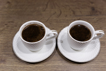 Two white cups with coffee on the table.
