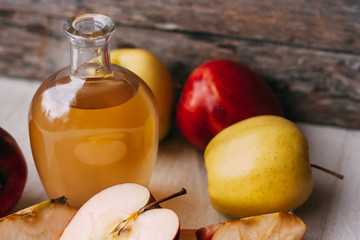 Apple organic vinegar in glass pitcher with ripe fresh red and yellow apples on wooden background. Healthy organic food concept