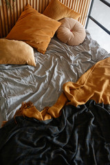 The bed is covered with a gray sheet, orange pillows and rugs of orange and black colors.