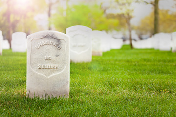 Tombstone of unknown soldier on the cemetery grass ground with other graves on background
