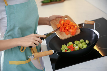 Young woman cooking on stove in kitchen, closeup