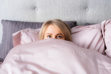 Obraz premium A woman peeks out from under the covers. The girl is hiding under the covers.
