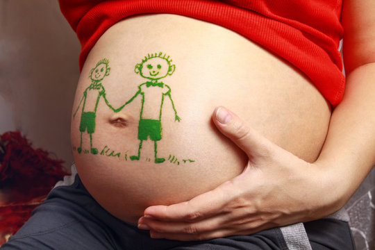 Pregnant with a big belly and a pattern on it. Images of two twin boys. Parents are waiting for twins .Stock photo
