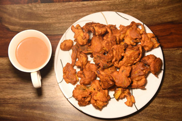 Chai with pakoras and bhajiyas and served on plate on wooden background