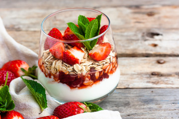 Yogurt with muesli and fresh strawberries for healthy breakfast or snack. Strawberry dessert parfait with yogurt and granola on a wooden table. Healthy and organic nutrition concept. Selective focus
