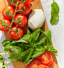 mozzarella, organic cherry tomatoes and fresh basil on a rustic wooden background