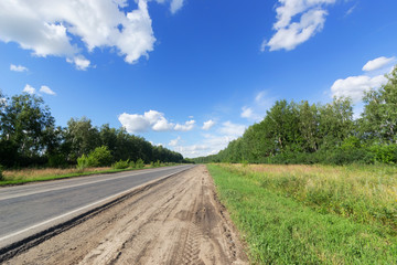 Fototapeta na wymiar Paved and unpaved road, among birch trees under a blue sky and white clouds