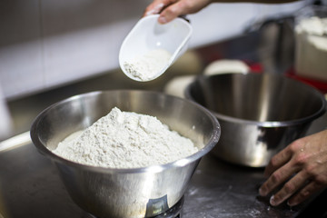 hand pouring flour into a metal bowl