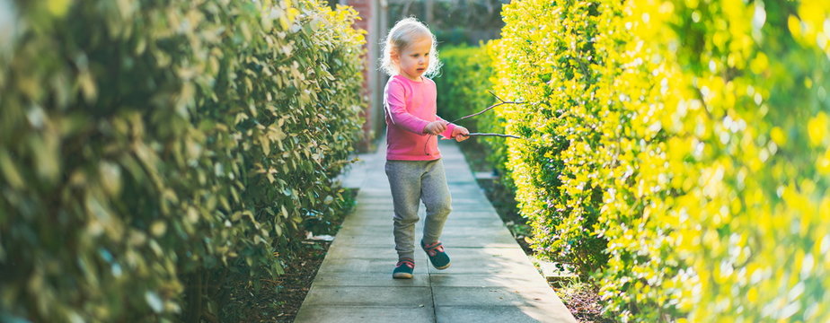 Happy small girl running in the park. Small girl playing with the rod. Toddler girl child running around and enjoying freedom on the pavement in the park. Warm vivid filter. Focus on hands. Small girl