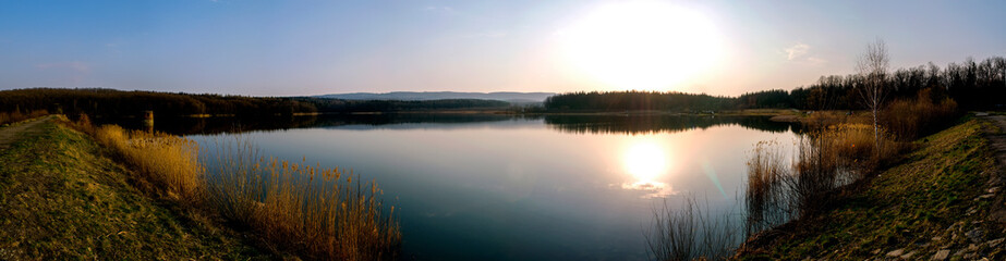 Beautiful spring sunset near lake with blue sky, green trees and water with reflection