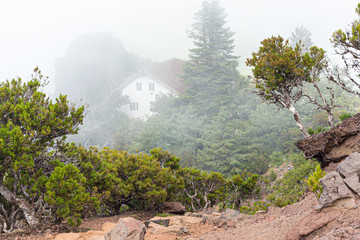 A white house with a tiled roof in the mountains among the clouds.
