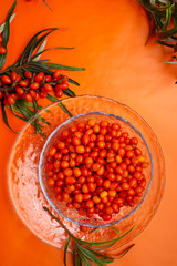 ripe sea buckthorn berries with branch around orange background.  flat lay