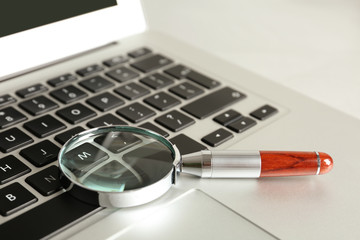 Magnifying glass and modern laptop on table, closeup. Search concept