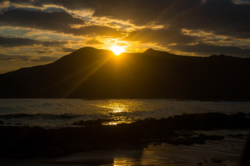 Amanecer y salida de sol desde atrás de una montaña ubicada frente a una playa