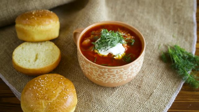 hot beetroot soup with sour cream, herbs and rolls in a ceramic bowl