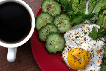 Traditional fried eggs with fresh cucumbers seasoned with spices with a Cup of coffee for Breakfast on a white background in a red plate