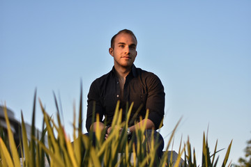 Man sitting in grass during sunset with blue sky and formal clothes