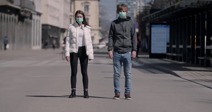 Portrait of young couple wearing medical masks in a city due to coronavirus outbreak. Two people with protective gear standing on a street and looking at the camera