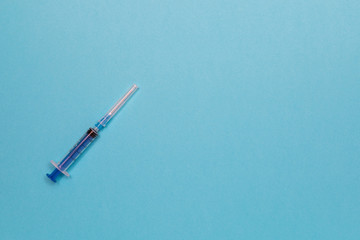 Syringe for injection with a needle on a blue background. Top view with copy space, flat lay.