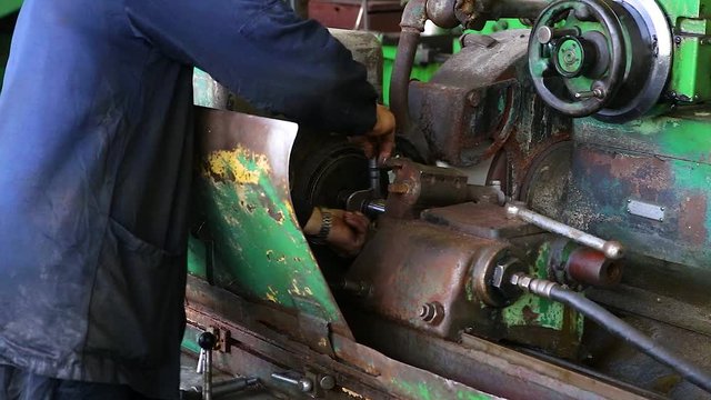 A blue uniformed worker measures a part in an old lathe. Close-up