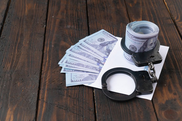 twisted wad of dollars buttoned with handcuffs on wooden background, envelope with money