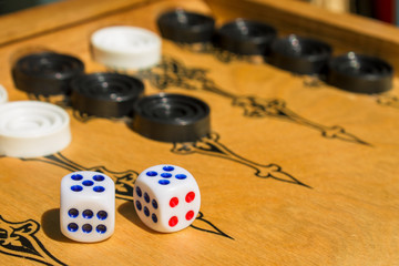 Backgammon, board game. Two cubes, lie on a wooden covering. Black and white details. Background in blur.