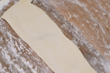 Strip of dough on a wooden board with flour. Cooking dough rolls. Homemade baking.