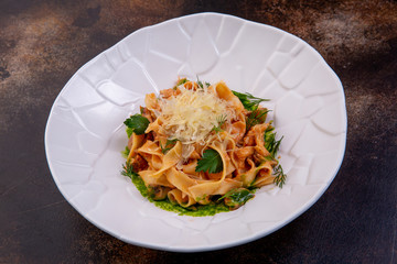 Pasta with chicken, mushrooms and sun-dried tomatoes in a white plate against a dark background. European cuisine. The work of a professional chef. Dish from a restaurant or cafe menu