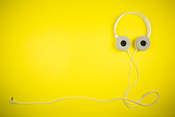 White audio headphones with a 3.5 mm wire on a yellow background
