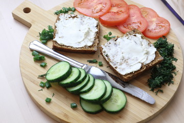 Healthy, fresh breakfast on a wooden board from slices of grain bread with cream cheese, slices of cucumber, tomato, on a light background. Proper nutrition, easy digestion, morning rituals, habit