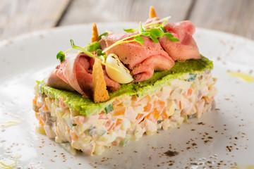 Russian traditional salad Olivier with vegetables and meat. Salad on a plate on a gray wooden background