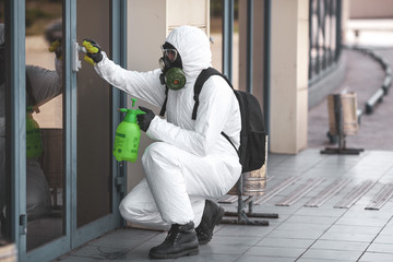 Quarantine, coronavirus infection. A man in protective equipment disinfects with a sprayer in the city. Cleaning and Disinfection at the street. Protective suit and mask. Epidemic.