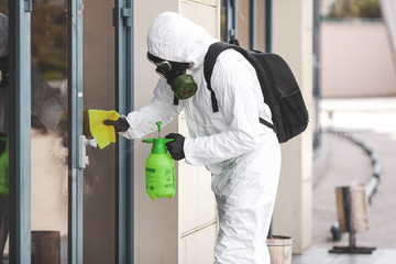 Quarantine, coronavirus infection. A man in protective equipment disinfects with a sprayer in the city. Cleaning and Disinfection at the street. Protective suit and mask. Epidemic.