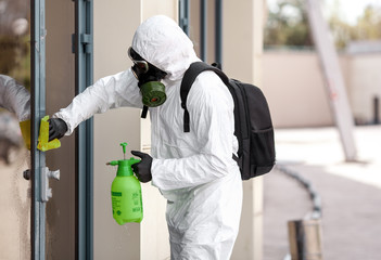 Quarantine, coronavirus infection. A man in protective equipment disinfects with a sprayer in the city. Cleaning and Disinfection at the street. Protective suit and mask. Epidemic.