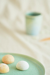 Three bright colorful mochis on a green plate and a coffee cup on a beige fabric.