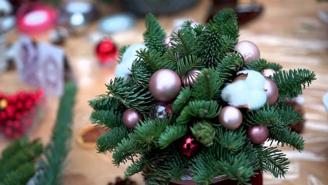 Christmas composition: a green pine tree branches, red, silver and pink christmas tree toys and cotton flower balls in a basket. Christmas decoration elements on a light wooden surface table, close-up