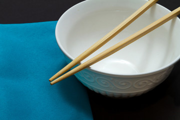 Chopsticks on a white empty rice bowl next to a blue napkin